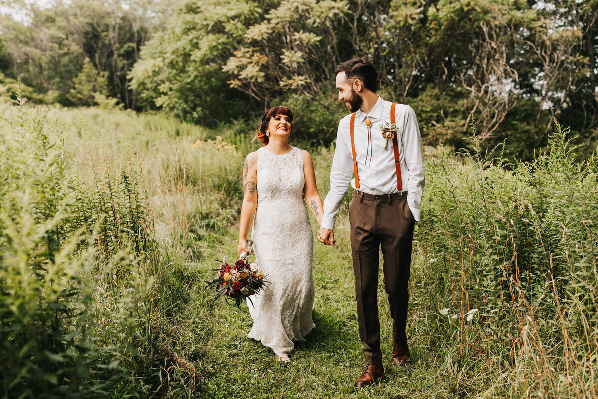 bridal couple walking through grass field holding hands