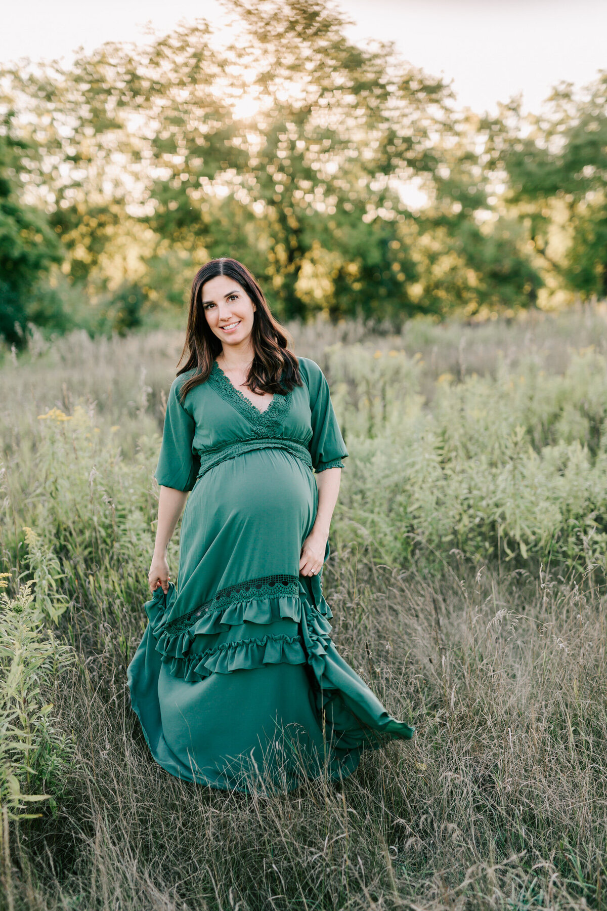 woman in green baltic born dress walks and swishes her dress in the grassy field during her maternity session with Toronto Newborn photographer Chelsey Kae Photography