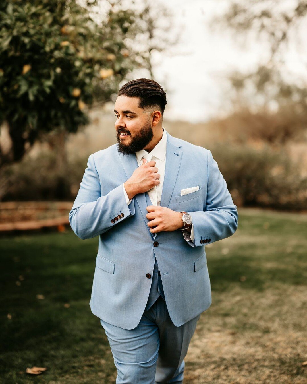 A man in a bespoke blue suit adjusting his tie