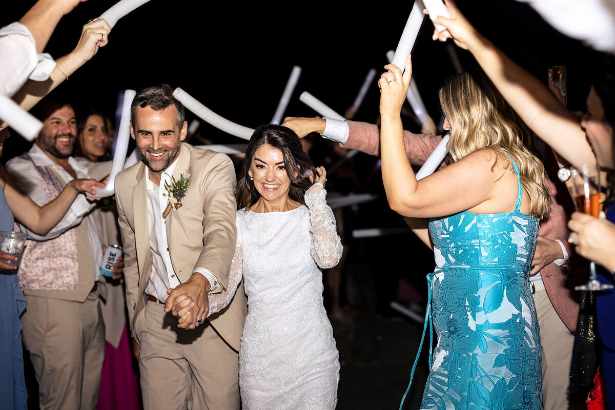 The newlyweds make a joyful exit through a tunnel of guests waving light sticks on a dark beach.