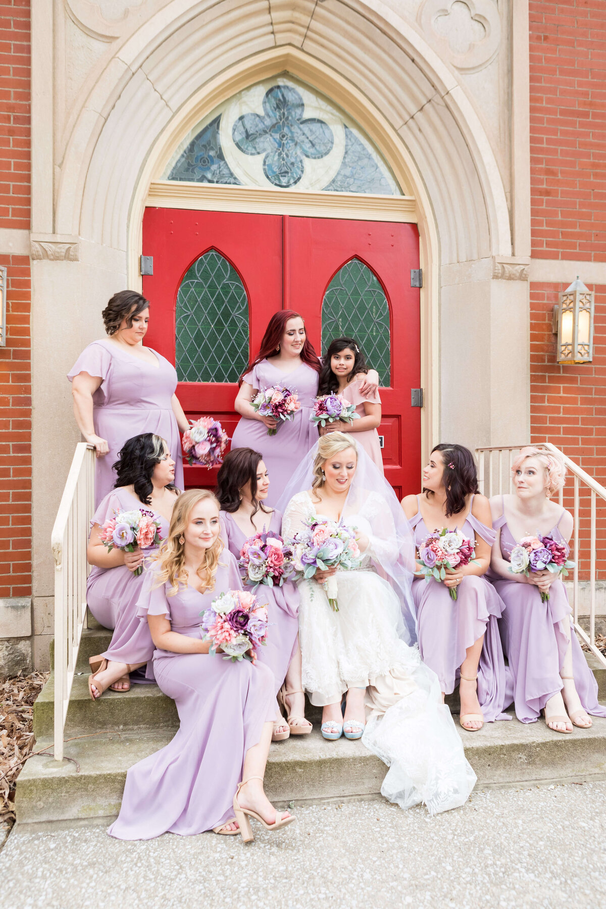 Bride sitting on steps surrounded by bridesmaids in purple dresses