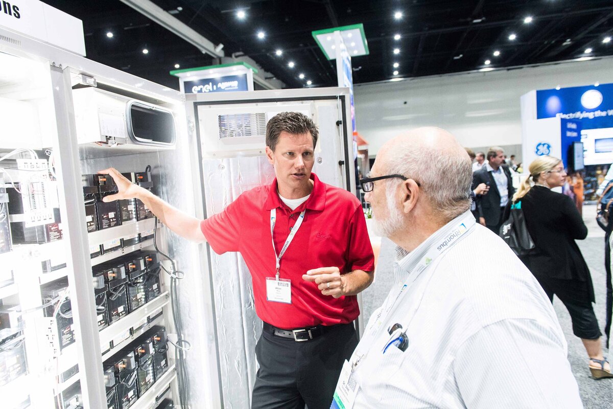 A sales rep shows another man a cabinet willed with batteries