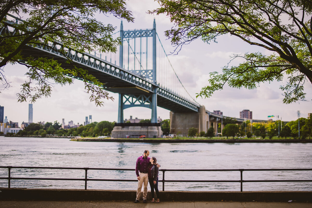 Engaged couple looking at each other at astoria park near the water with the RFK bridge in the back