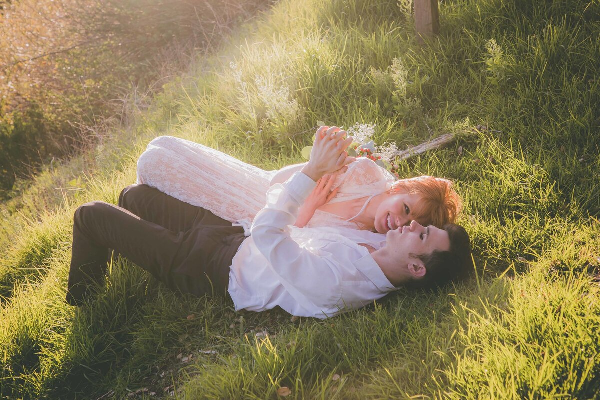 Couple lays down in grass and laughs.