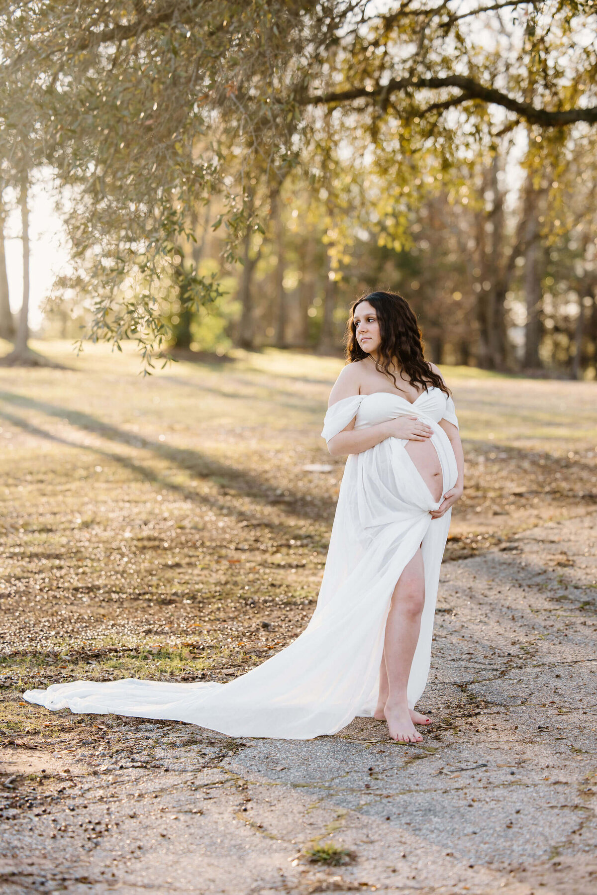 Maternity photo of pregnant mother in long white dress standing under large tree