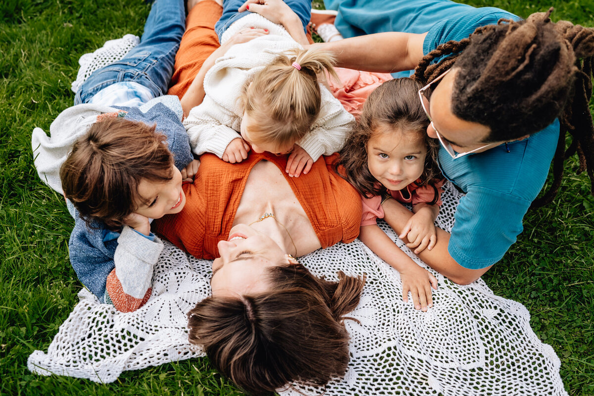 A family of five lays outdoors in the grass.