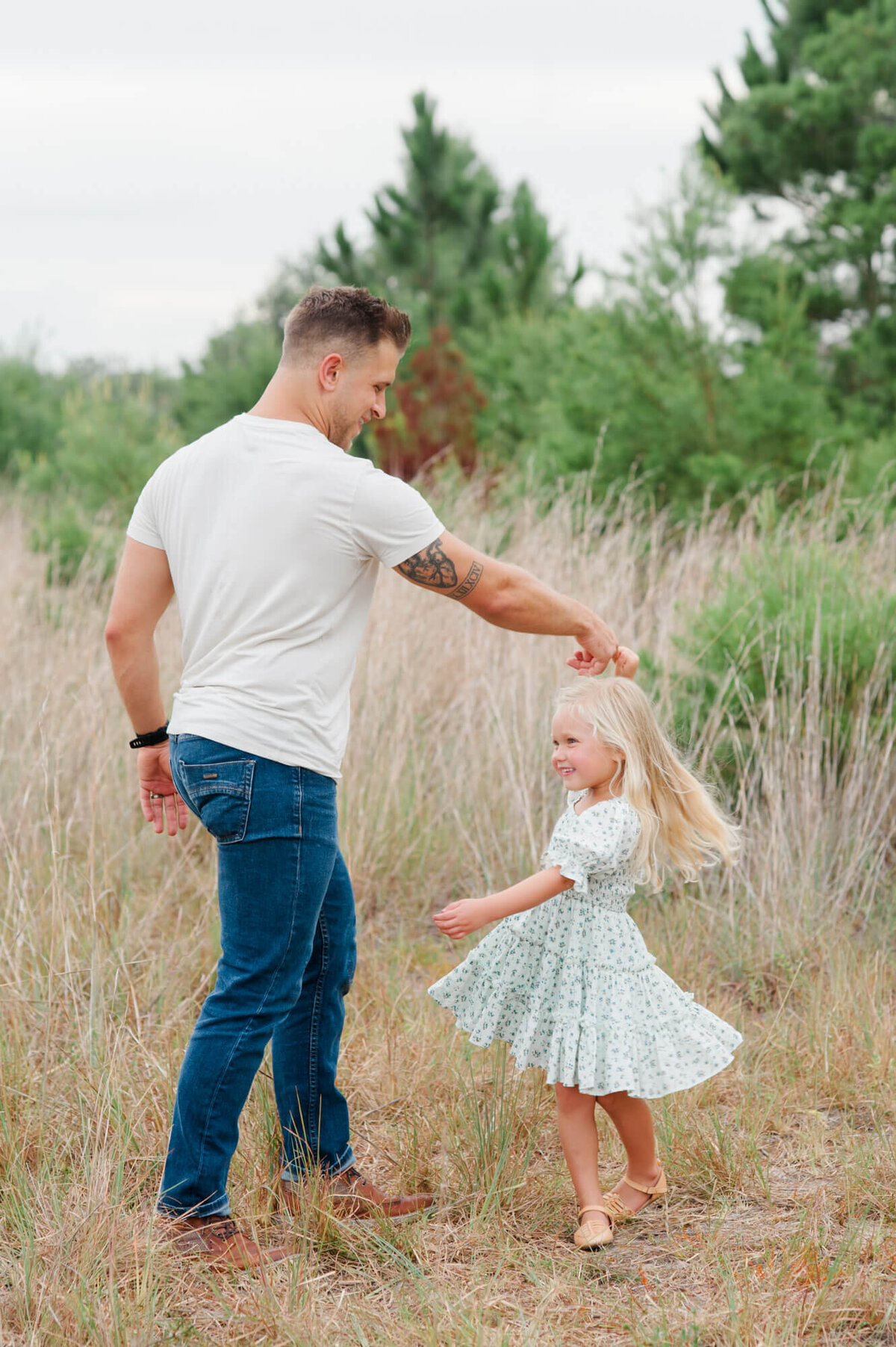 Dad spinning his young daughter while dancing with her in a tall grass field