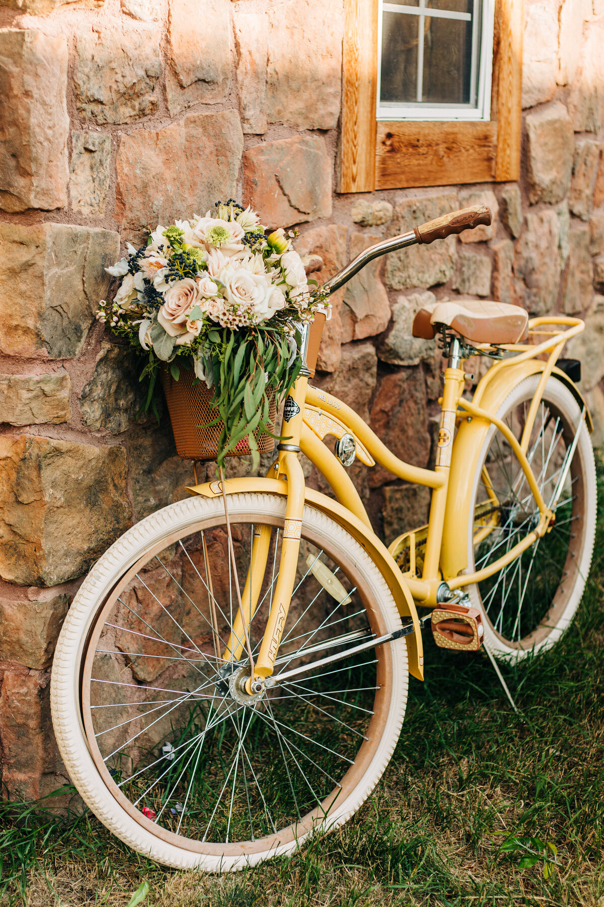 A bridal bouquet sits in the basket of a yellow bicycle during a Colorado Wedding.