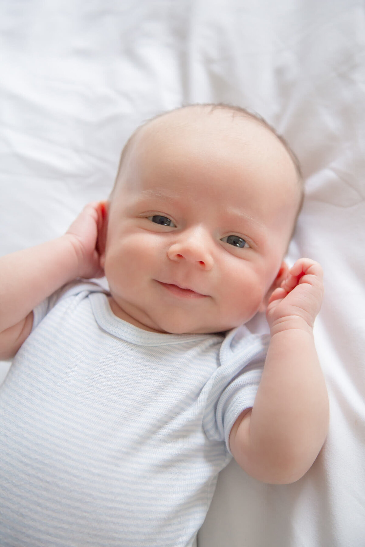 Stunning baby boy looking right at you laying on a white bed