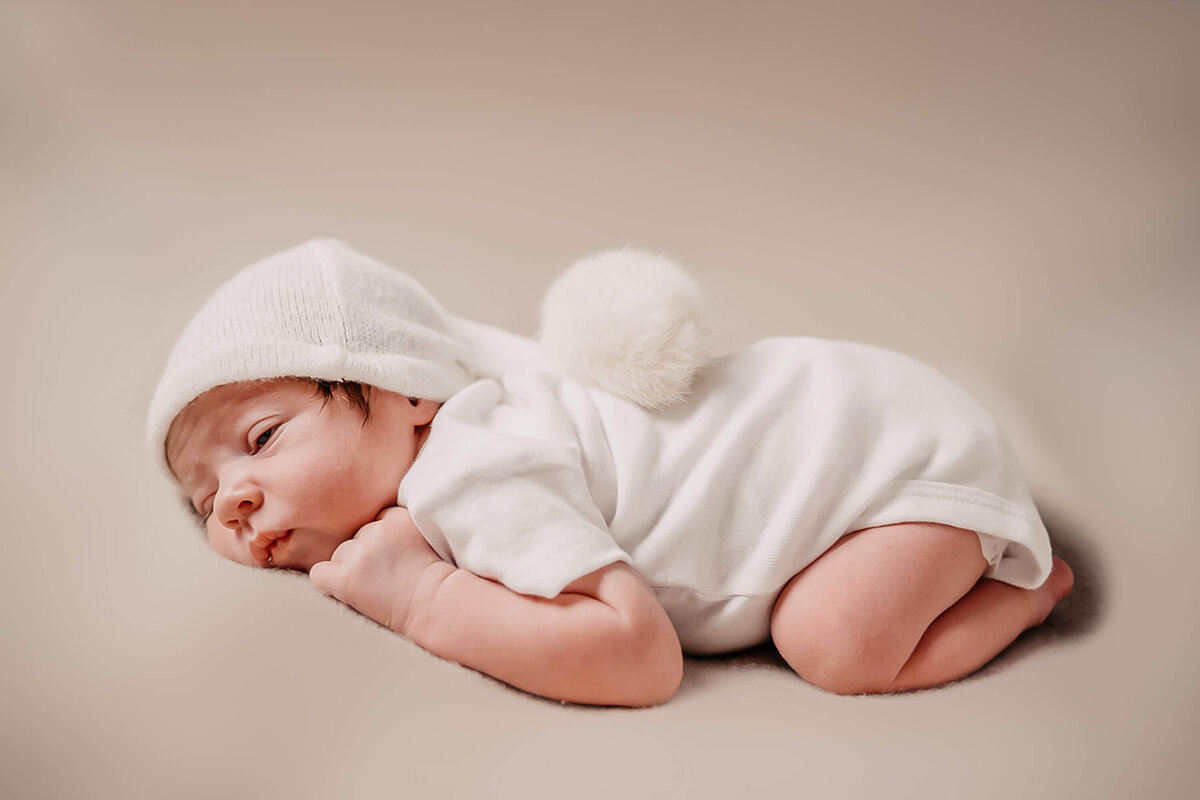 posed newborn baby sleeping on a cream blanket wearing a sleepy hat - Townsville Newborn Photography by Jamie Simmons