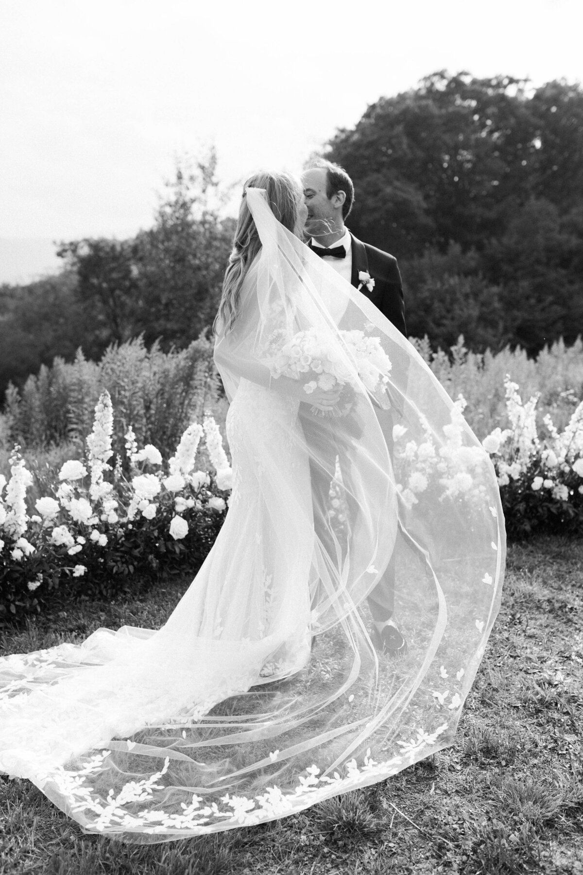 Bride's veil blows in the wind as the couple kisses 