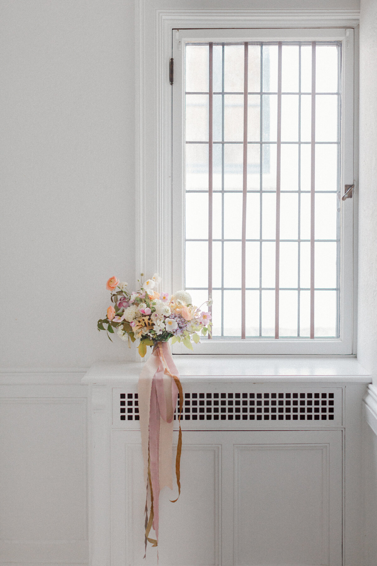 A springtime bridal bouquet tied by long pink ribbon sits on a windowsill at Livart. 