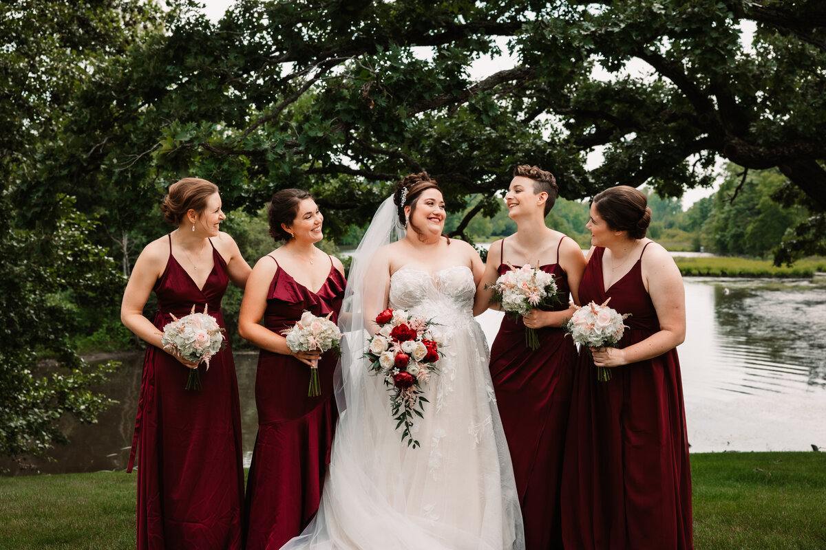 A bride laughs with her bridesmaids in a lawn by a pond