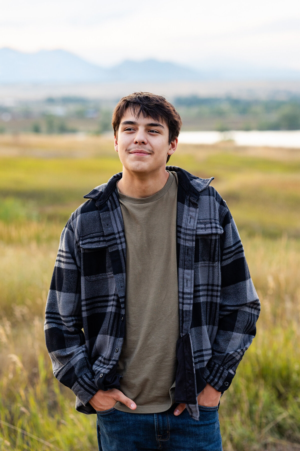 A senior boy looks off camera and smiles with mountains in the background.