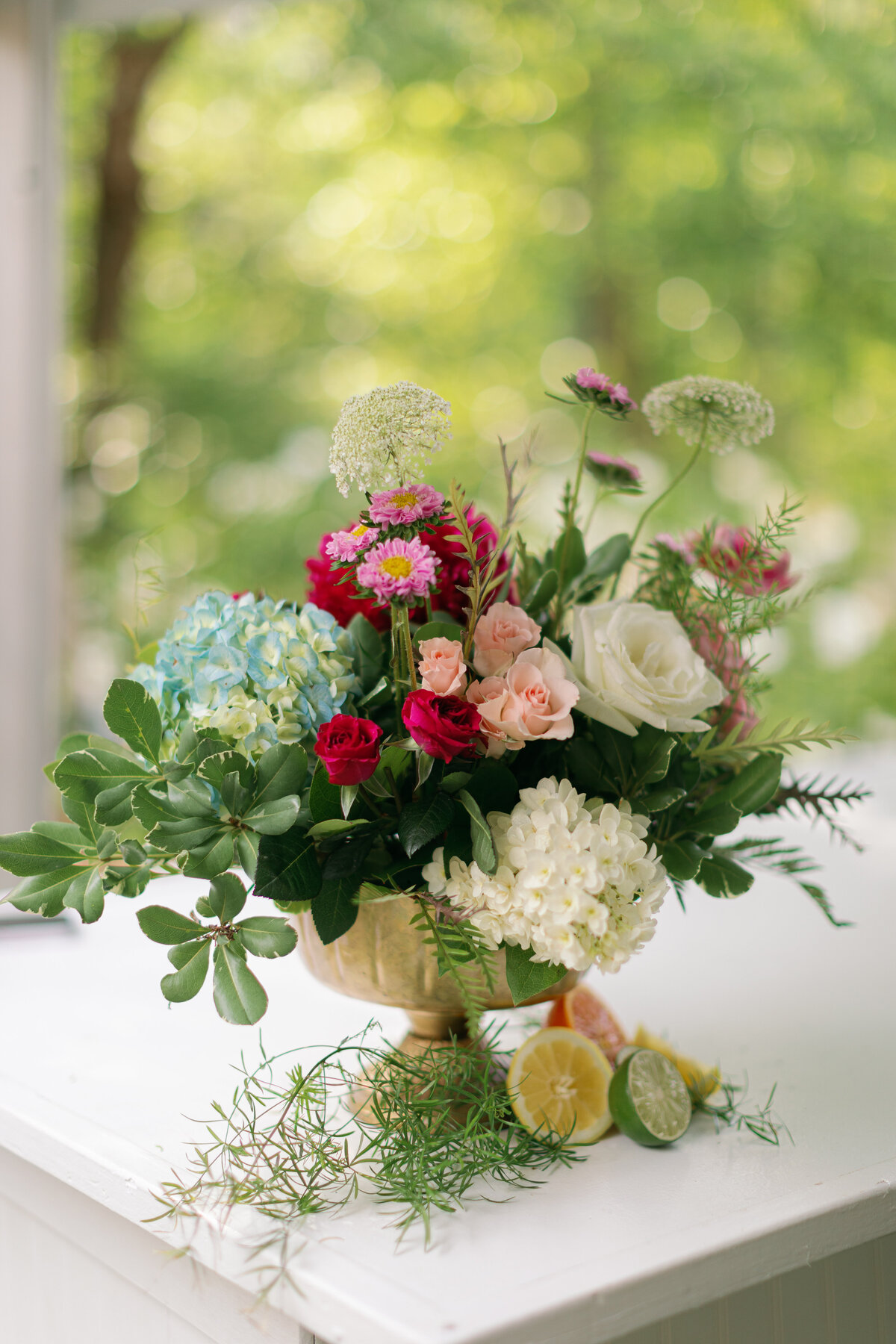 Colorful floral arrangement in brass vase with citrus fruit
