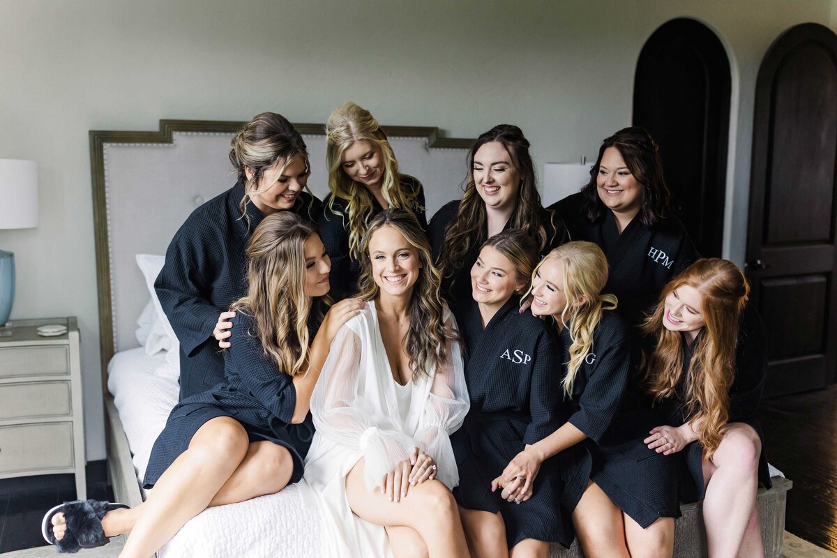 Bride sitting on bed surrounded by her bridesmaids posing for Chateau Selah wedding photographer