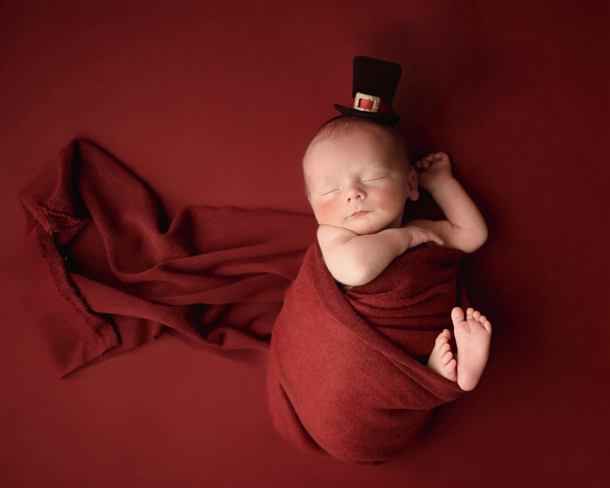 An Iowa Newborn Photographer shoots a sleeping baby swaddled in red