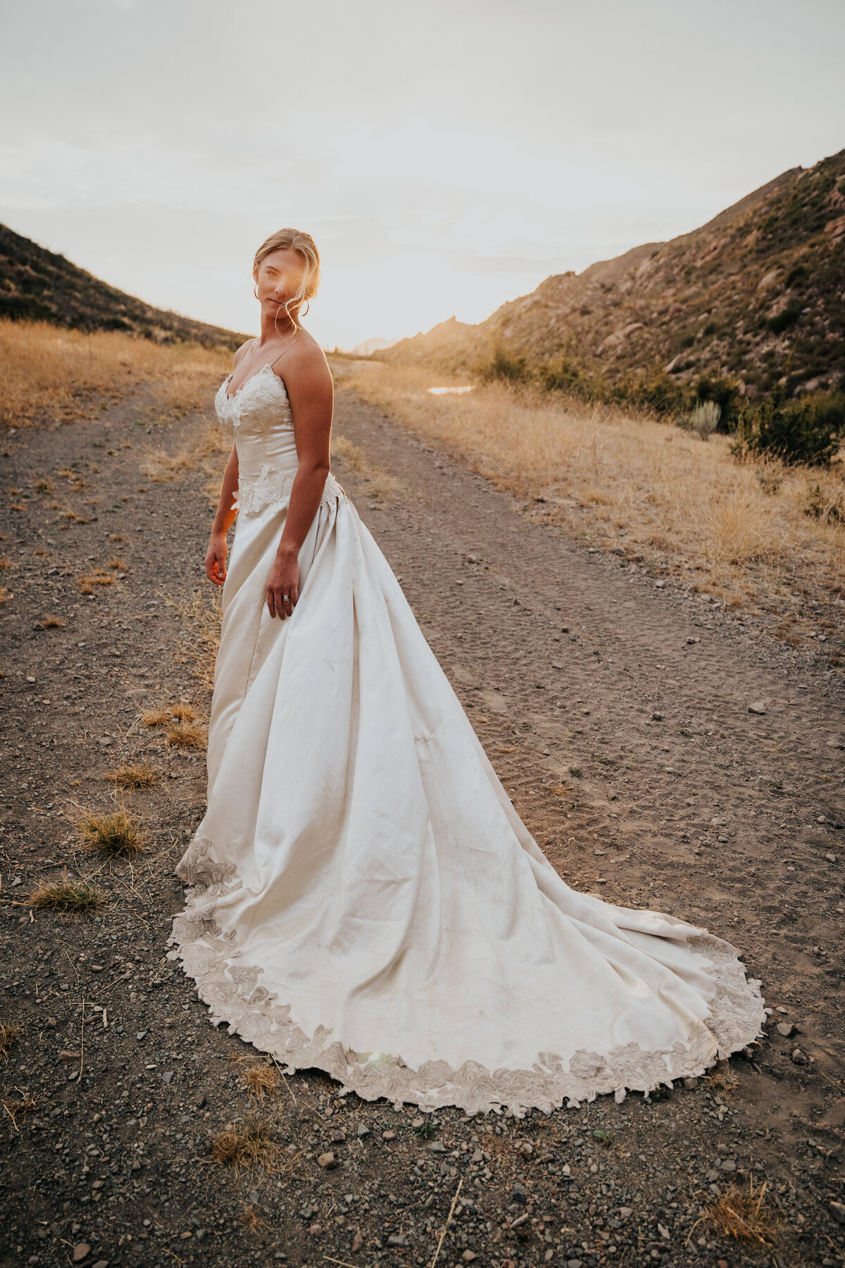Bride stands in front of sunset while wind tousles her hair.