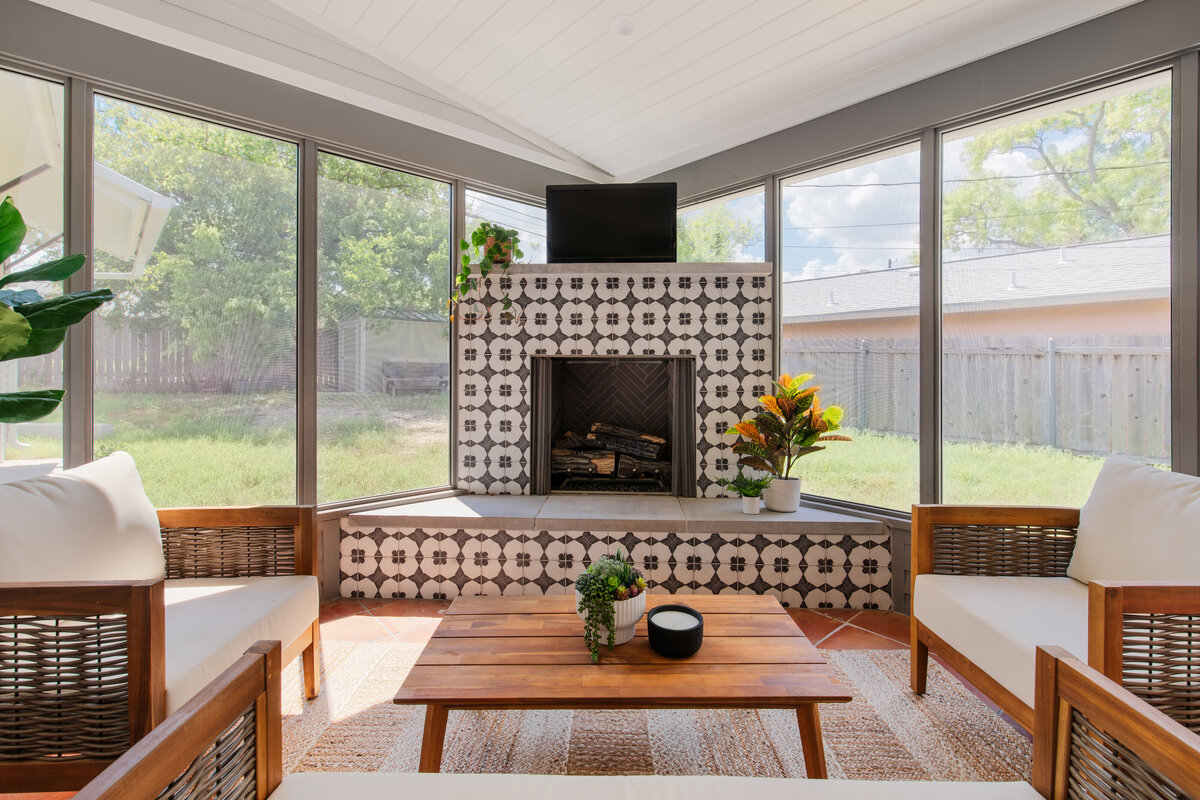 A screened sunroom with a beautiful tiled fireplace, teak outdoor furniture and wicker