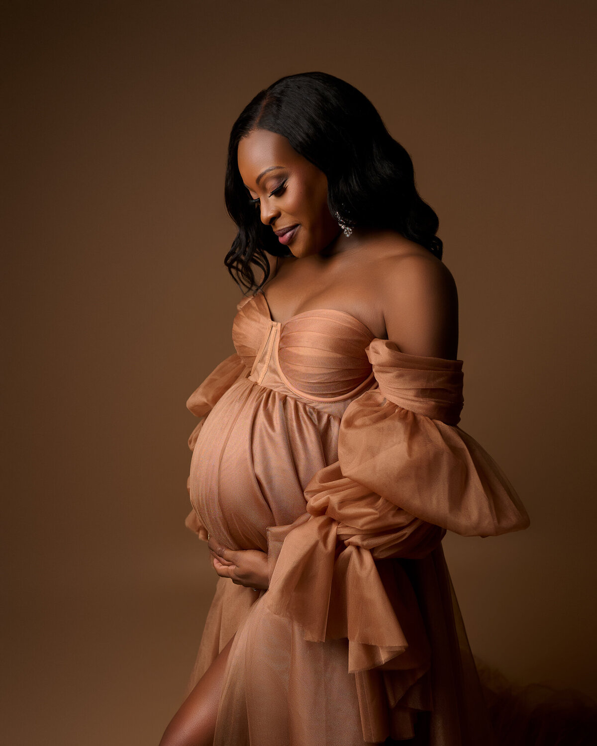 Warm studio maternity photo with soft brown gown and natural smile in Austin area