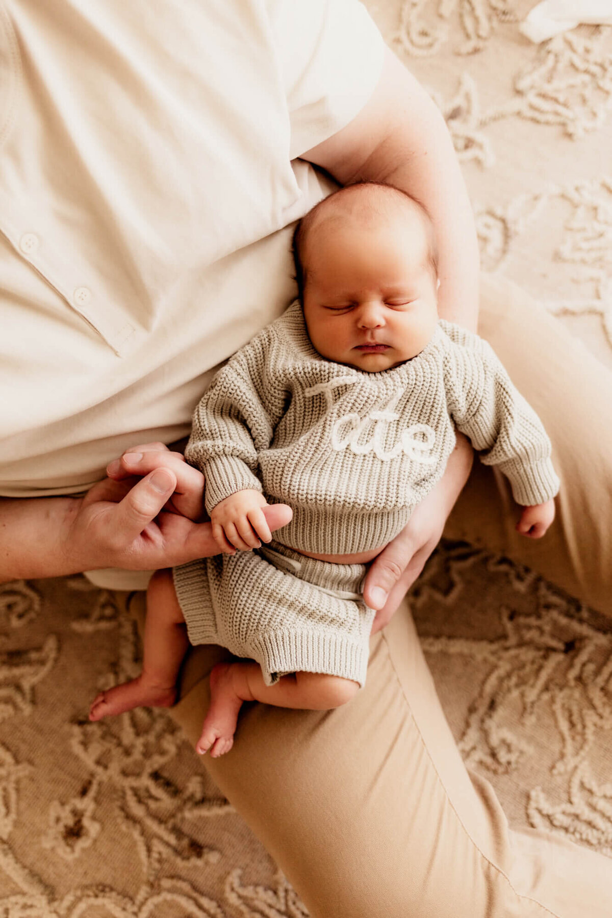 Father holds his son's hand on his index finger while cradling him for a newborn photo session in Oklahoma City.