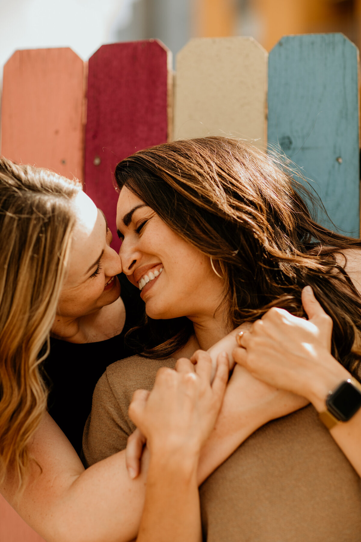 same sex couple hugging in front of a rainbow fence