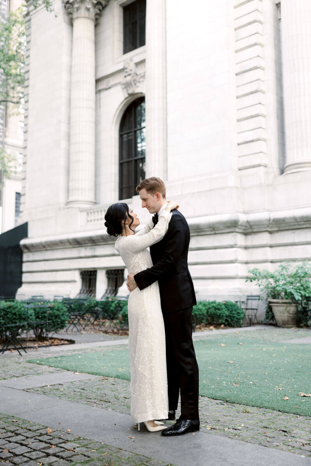 The bride and the groom are romantically holding each other close in front of the New York Public Library. Image by Jenny Fu Studio