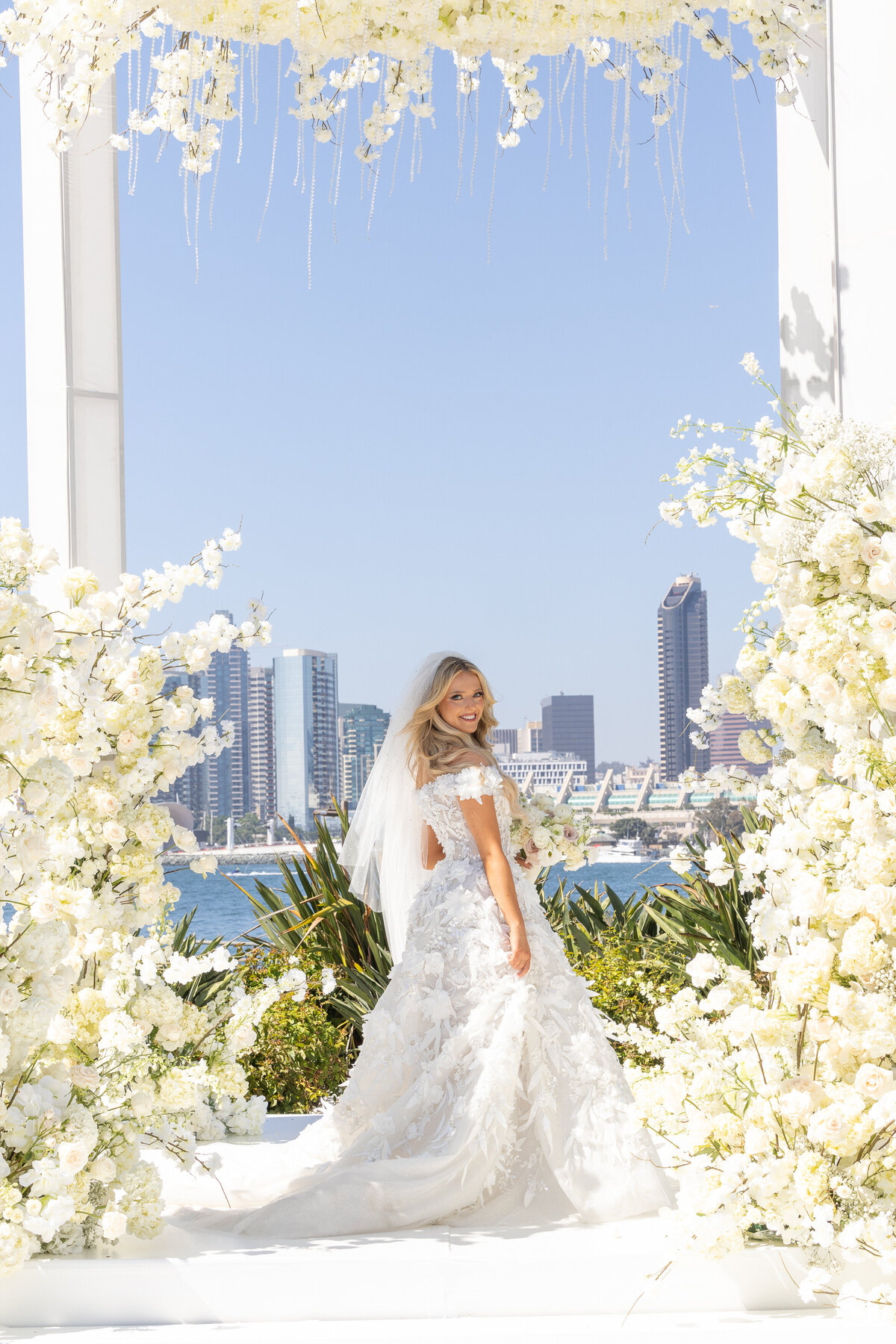 A bride standing surrounded by flowers looking over their shoulder