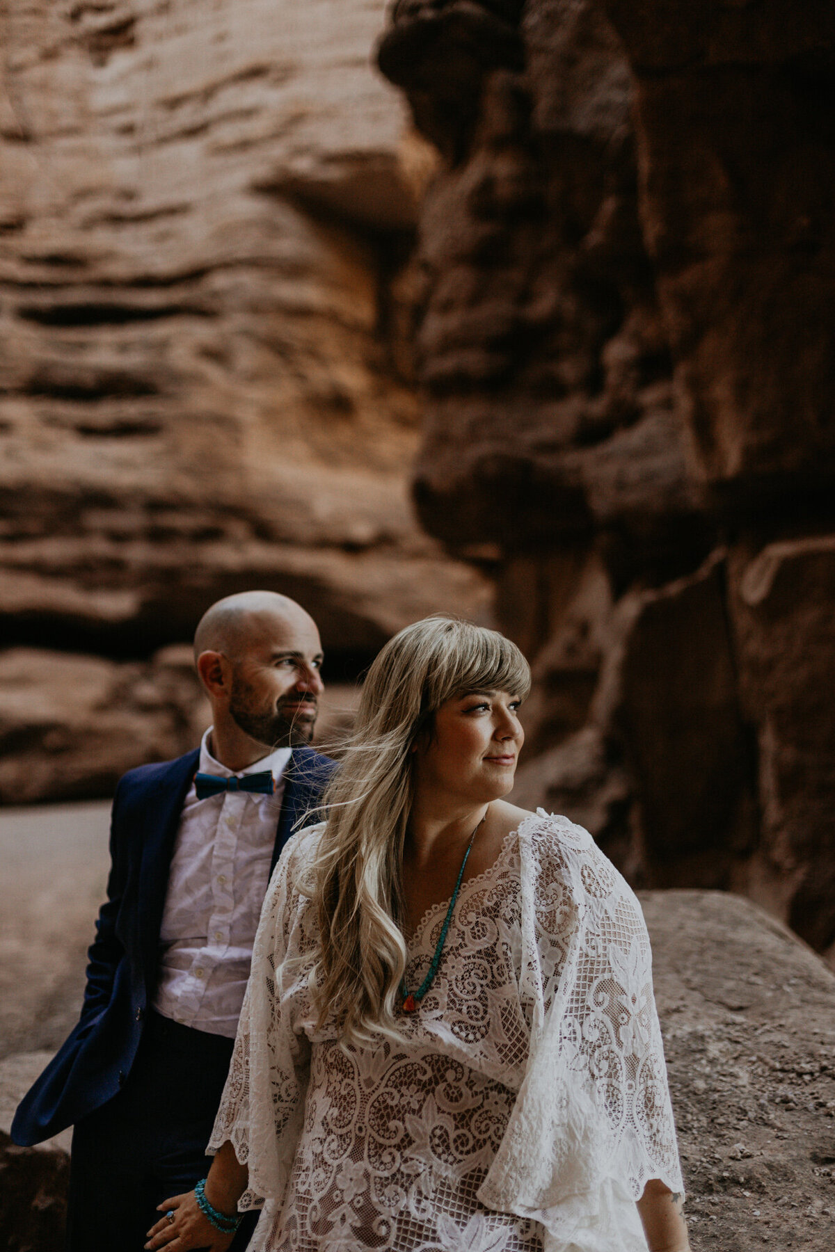 bride and groom sitting together looking off in a slot canyon