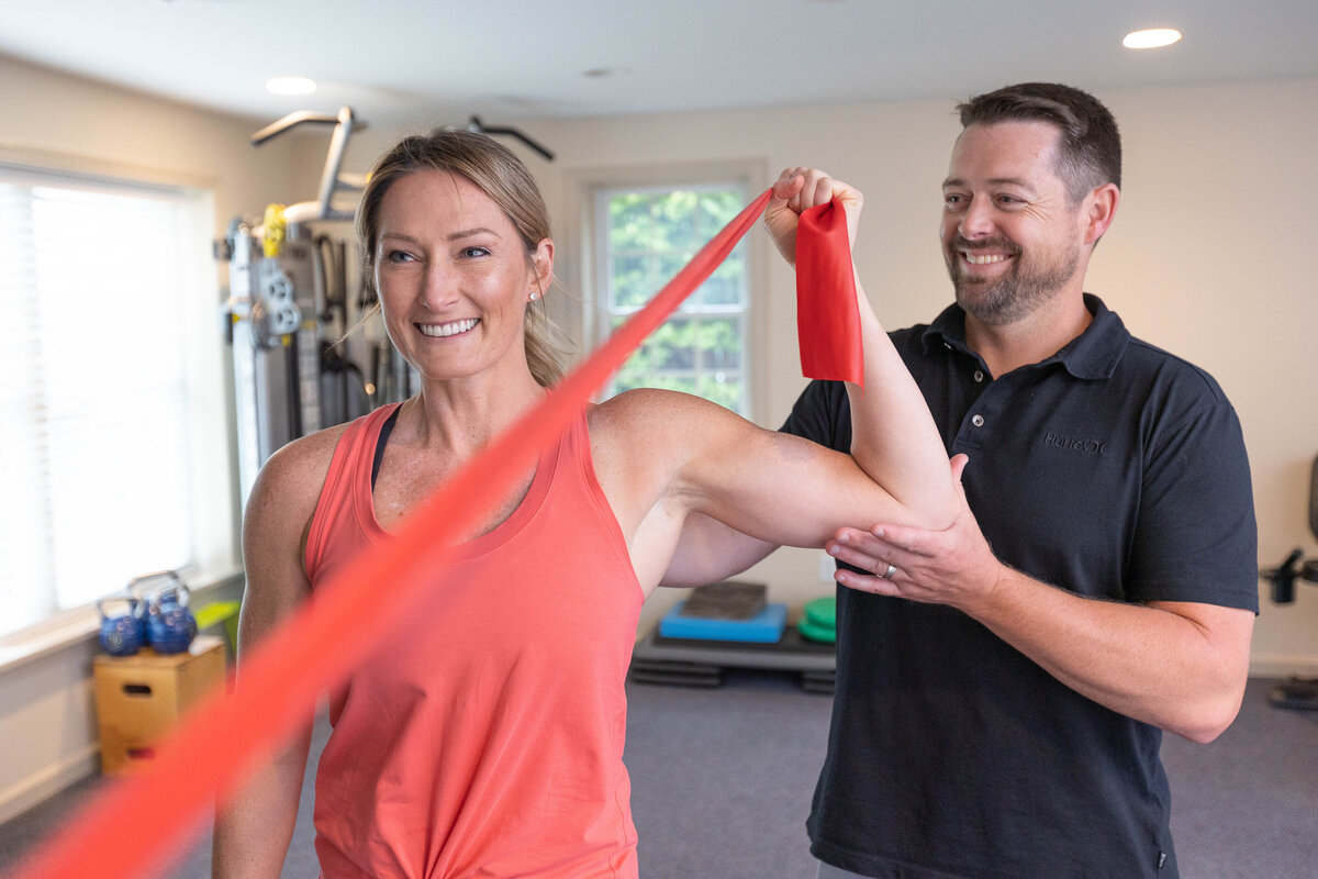 Physical trainer helping a smiling woman do exercises with an arm band