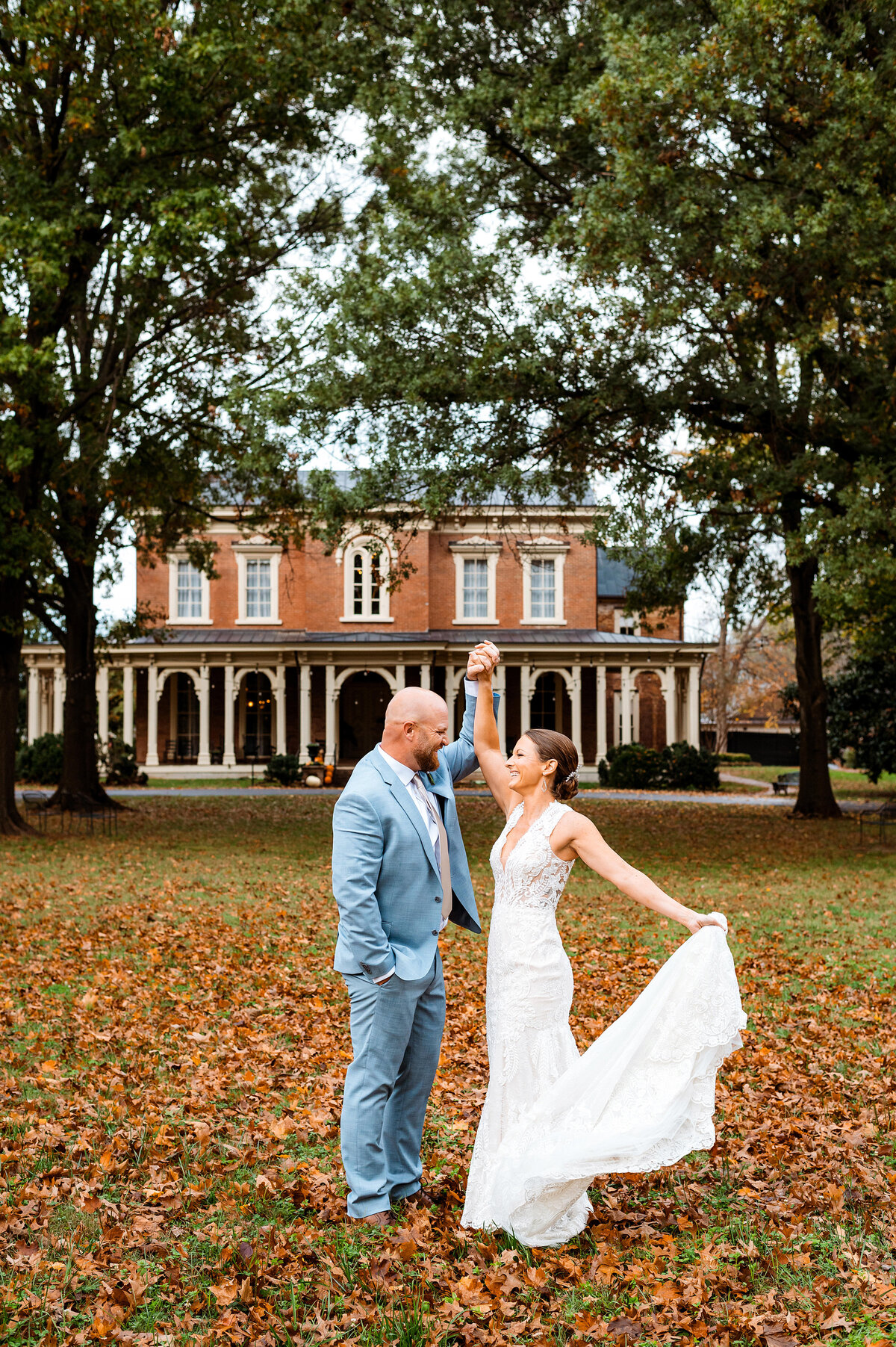 Bride spinning in dress with groom outside of Oaklands Mansion in the fall