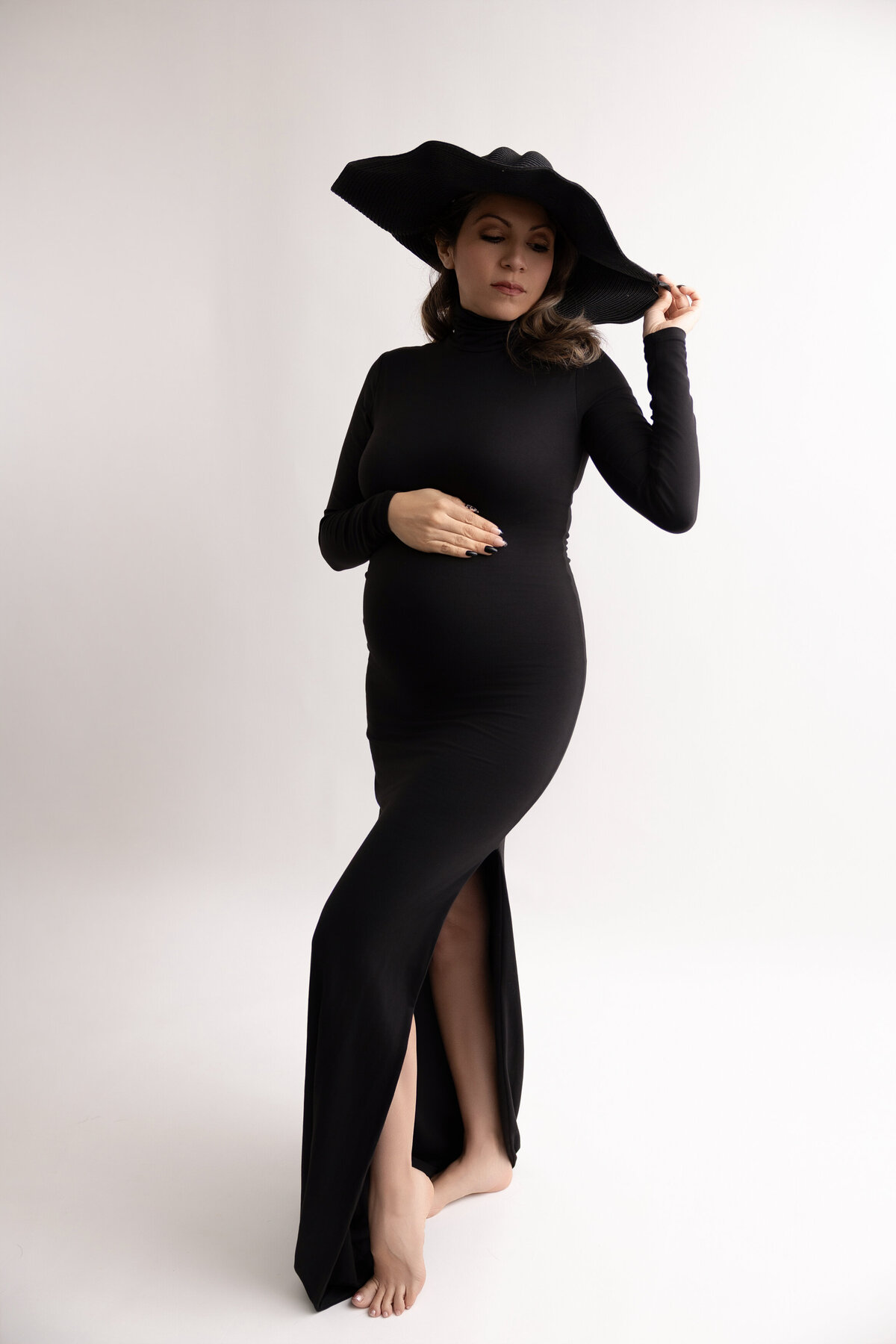 full length photo of pregnant woman wearing a fitted blak long dress and black summer hat.