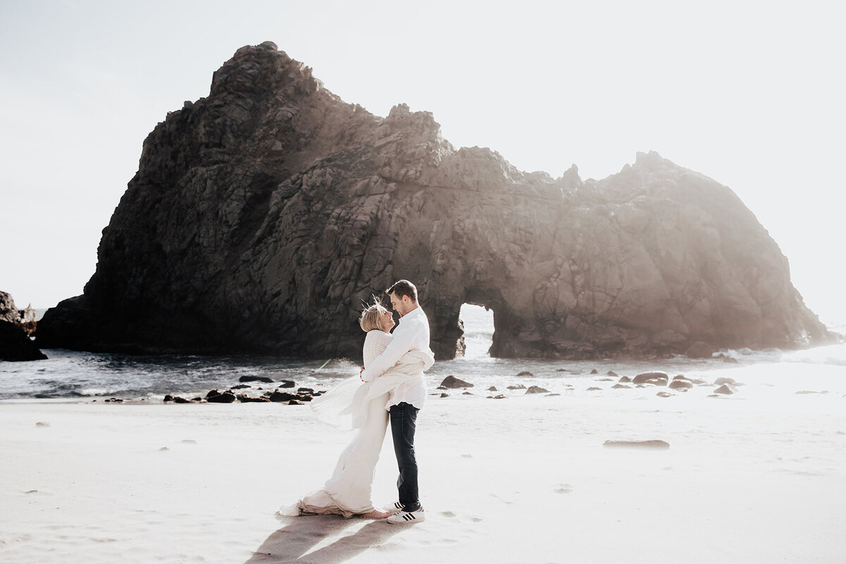 Wedding couple hugging in front of big rock formation in the ocean