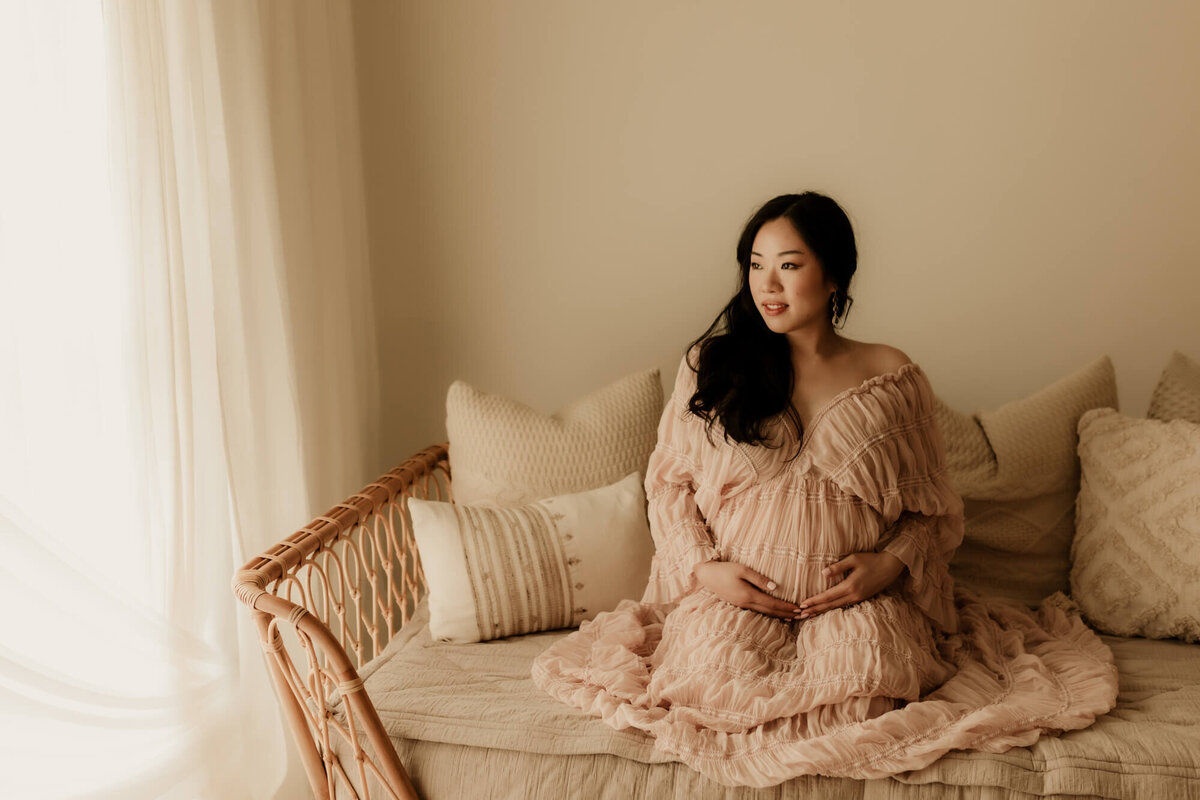 Maternity portrait of a mother wearing a blush dress while sitting on a daybed in OKC.