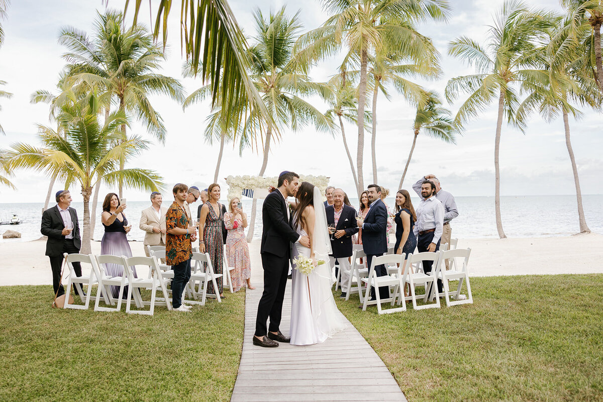Minette and Evan share a sweet kiss while family and friends cheer after their wedding ceremony. Florida Keys micro wedding by Claudia Amalia Wedding Photography.