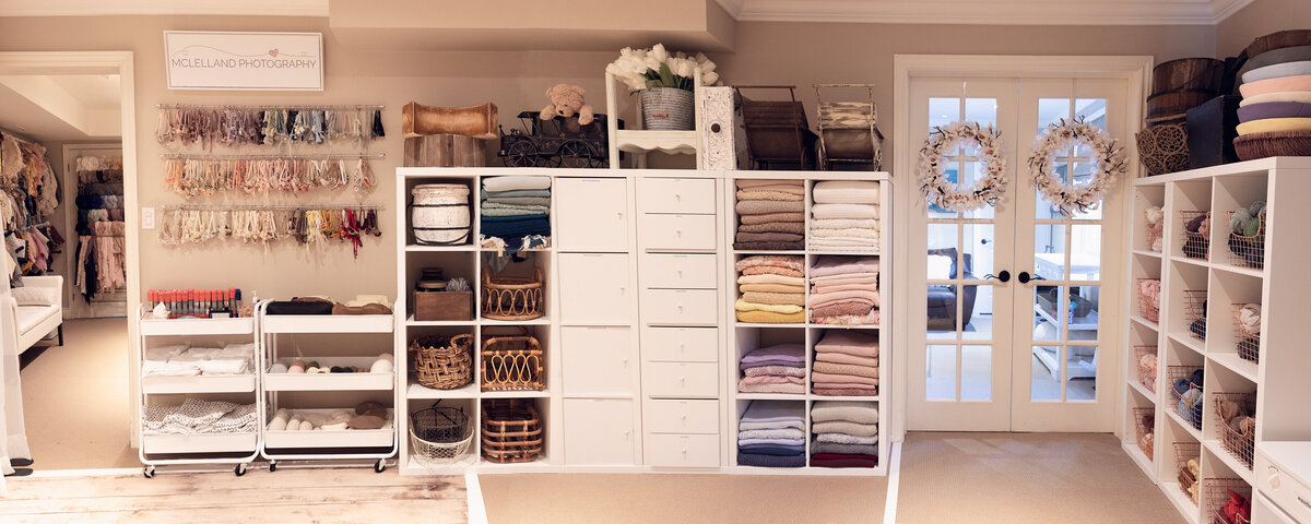 Wide-angle view of custom shelving, organized studio props, and the entrance doors inside a GTA newborn photography studio.