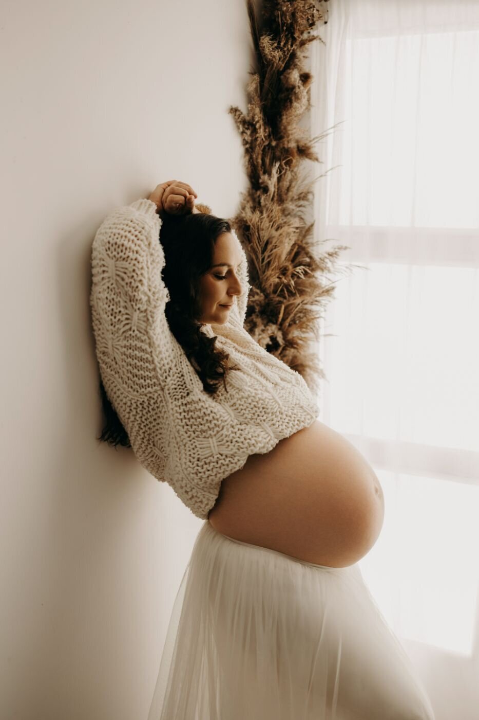 Serene maternity portrait of an expectant mother in a textured white outfit against a light wall
