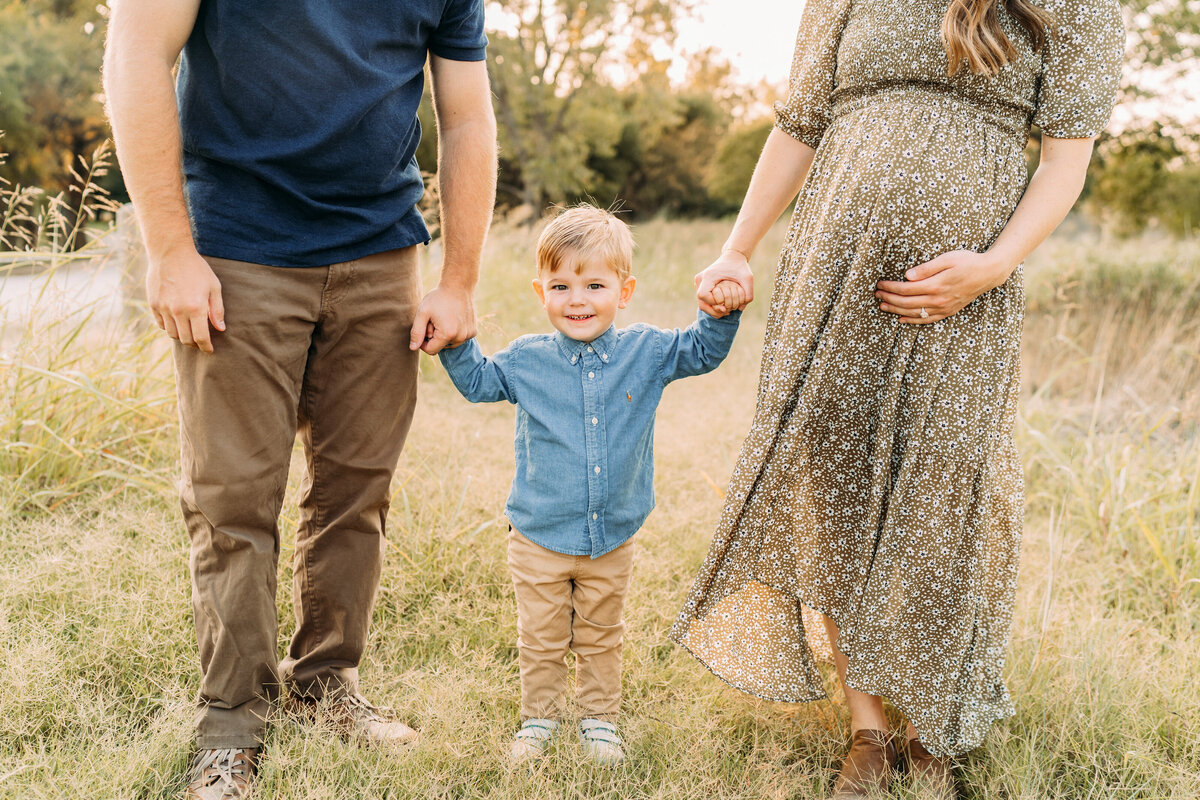 parents hold little boy's hand in a field during a maternity session