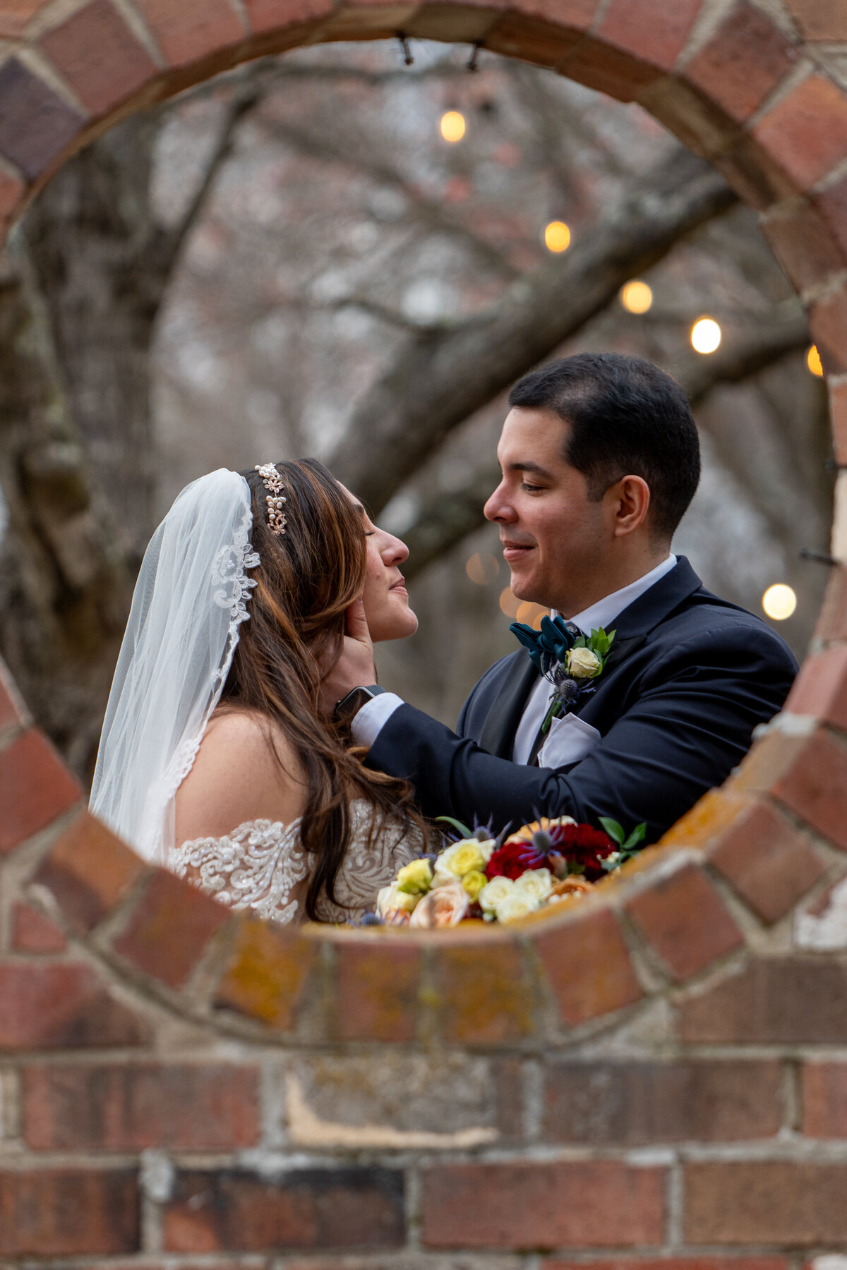 View of a wedding couple about to kiss through a circular hole in a brick wall 