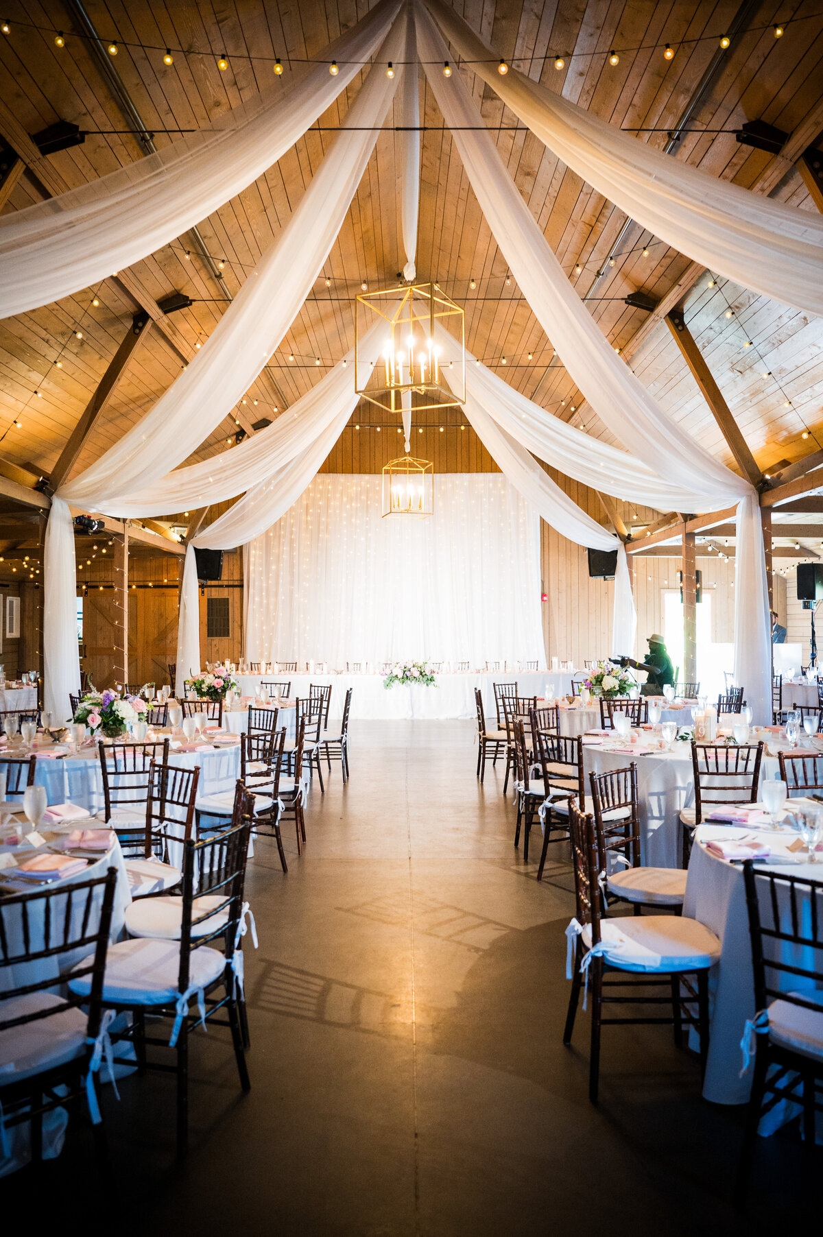 A wedding reception space is adorned with twinkle lights and white fabric draping the ceiling.