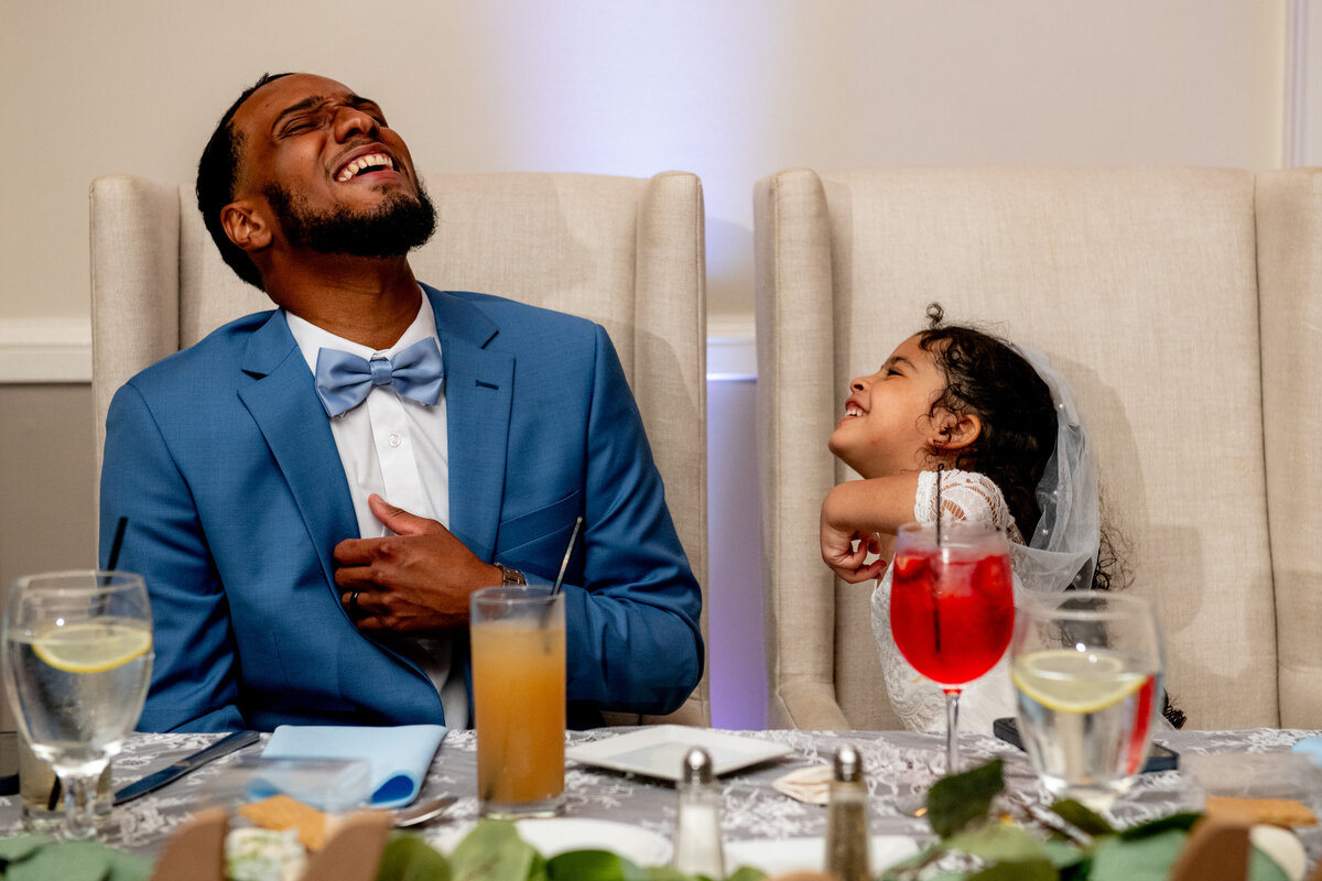 A man and a little girl laughing at a wedding reception.