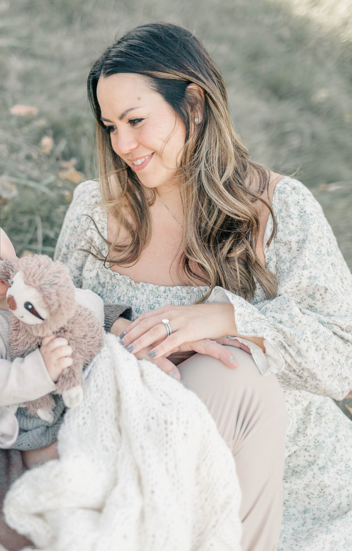 Portrait of a mother sitting wrapped in a cozy blanket with her baby during her first birthday photo session in a Kansas City park.