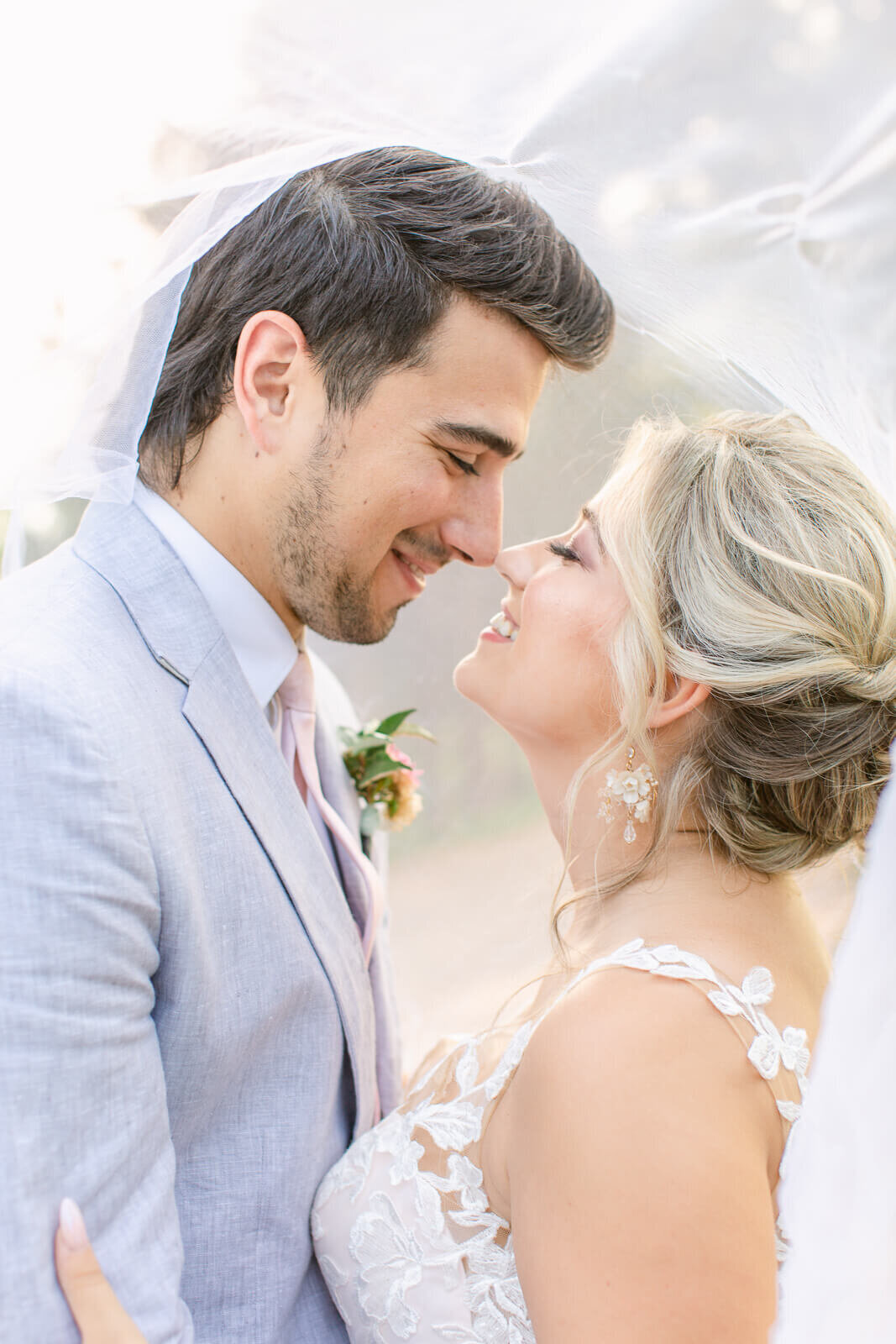 Bride and groom nose to nose under veil during wedding portraits. Captured by Bethany Aubre Photography.