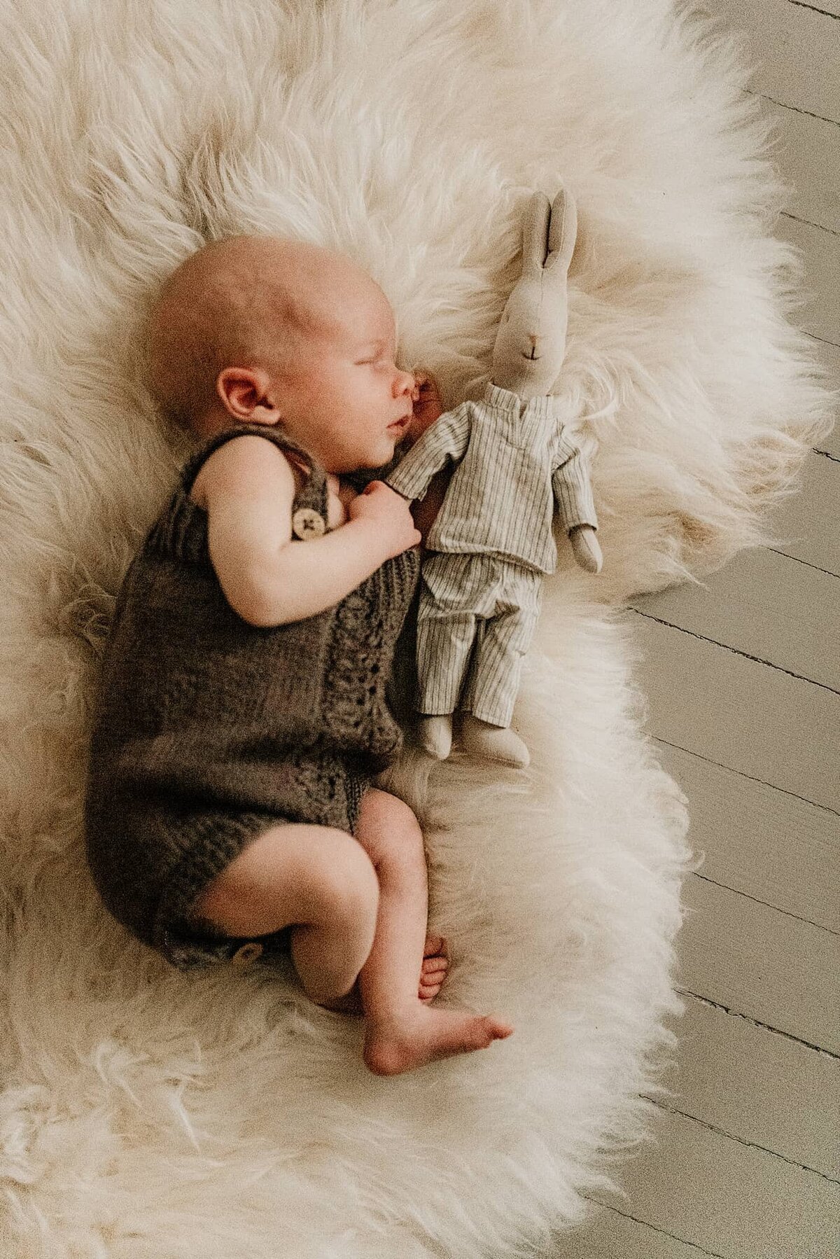 En nyfødt gutt ligger på saueskinn og sover under nyfødtfotografering.