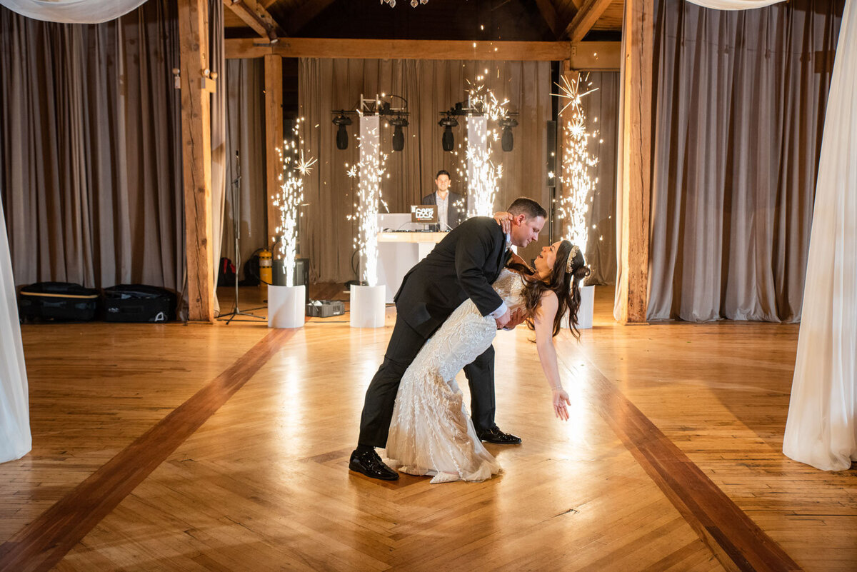 A bride and groom are dancing on a wooden floor with sparklers in the background.