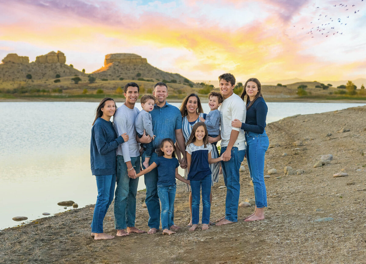 family of eight standing on a the beach at the Pueblo Reservoir at sunset holding hands