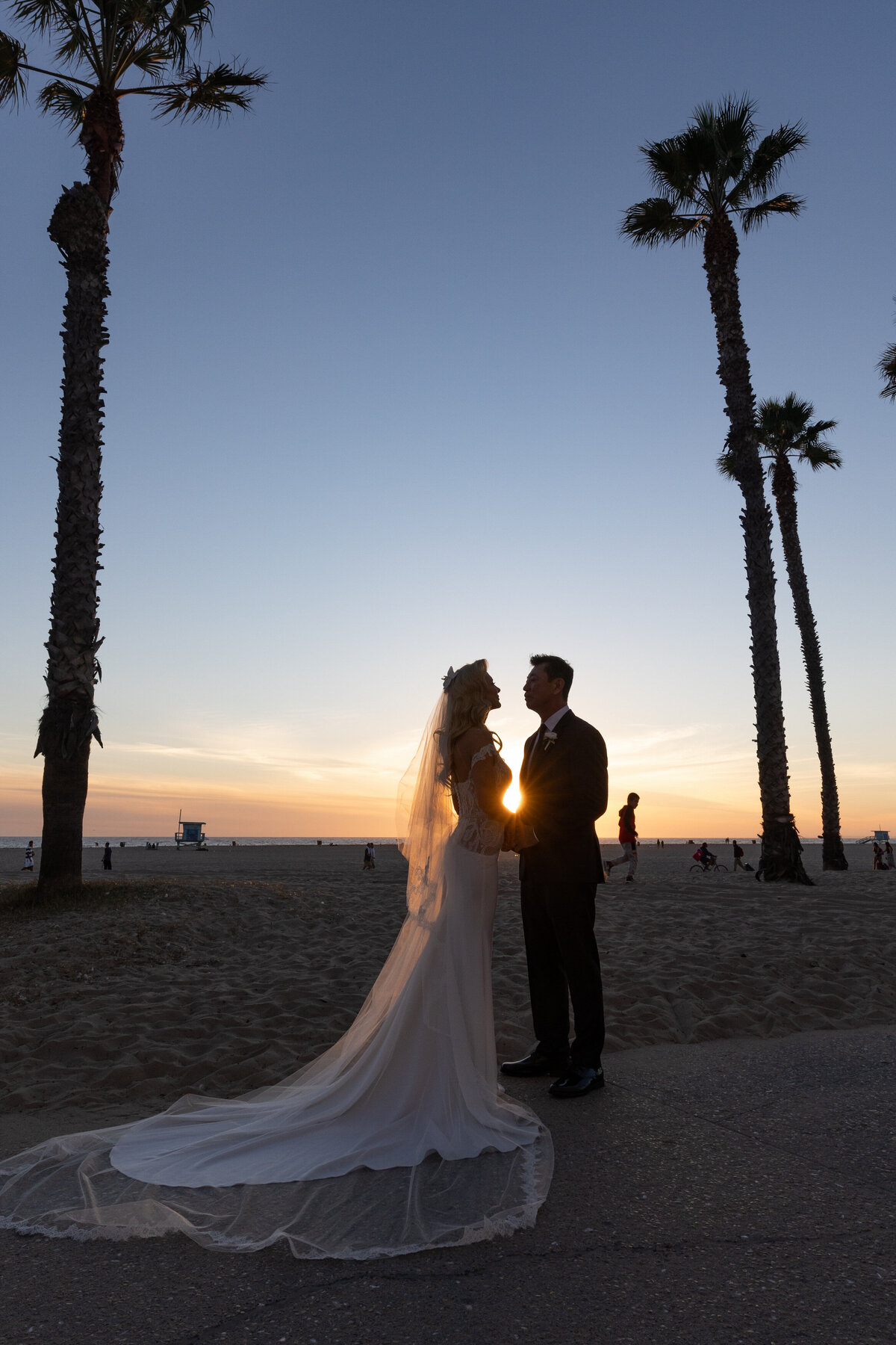 A bride and groom standing along the beach at sunset