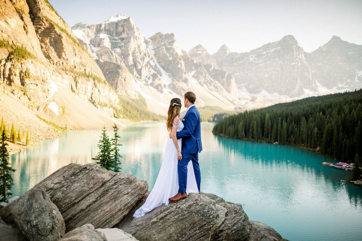 Moraine-Lake-in-the-distance-as-a-bride-and-groom-look-out-toward-the-Valley-Of-The-Ten-Peaks