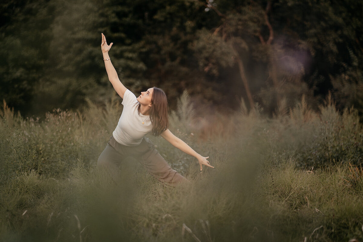 Tessa Adrian in einer Yoga-Pose auf einem Feld, Natur im Hintergrund.