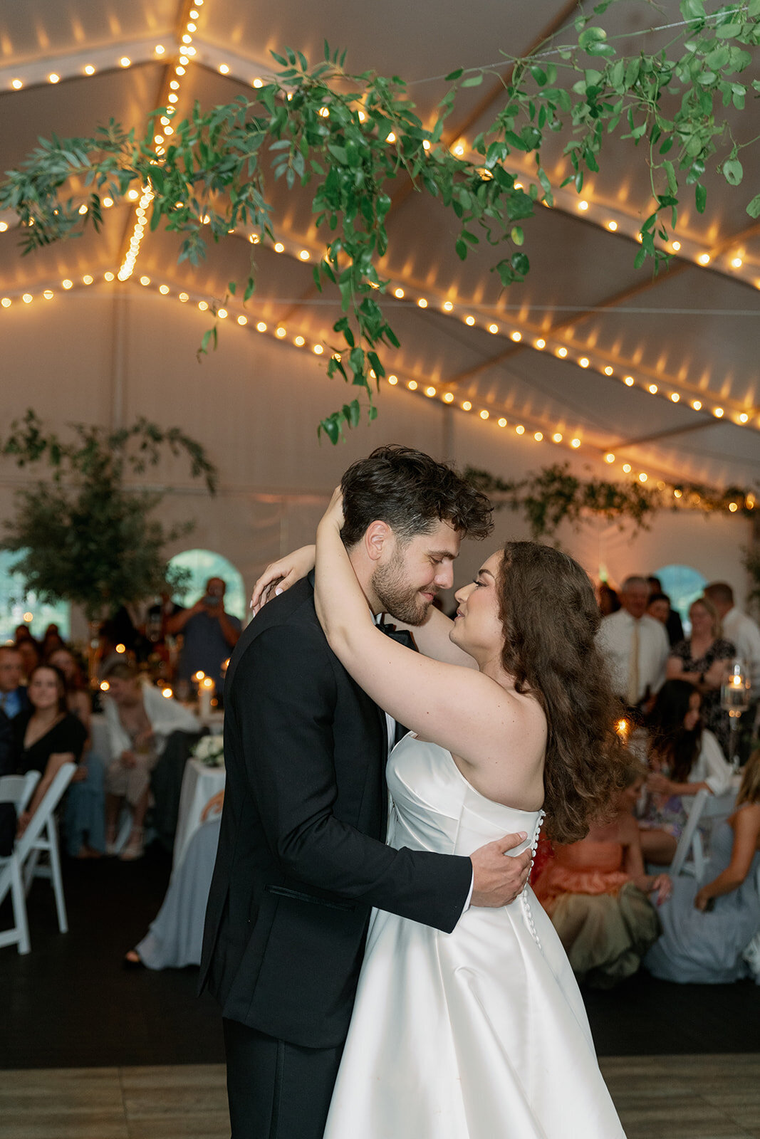 Wedding couple sharing their first dance under greenery and string lights at The Morris Estate reception tent.
